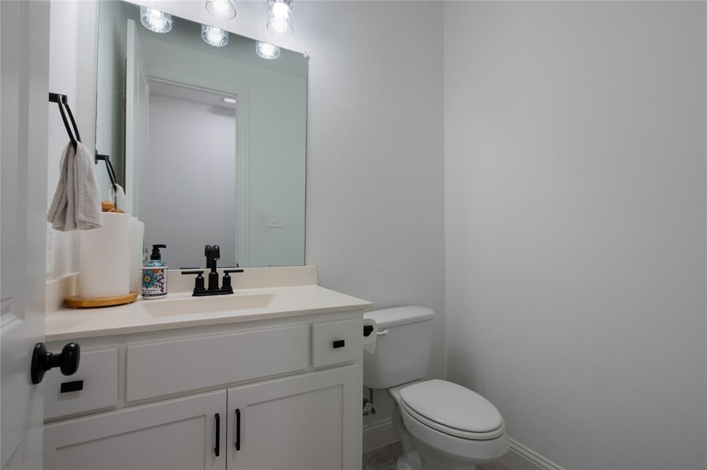 White vanity cabinet featuring a solid-surface countertop, rectangular integrated sink, matte black faucet, and matching cabinet hardware, paired with a large wall-mounted mirror and integrated vanity lighting