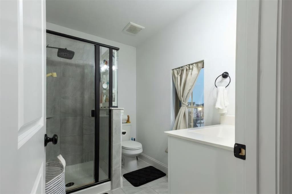 Bathroom featuring a glass-enclosed shower with dark-toned hardware, white cabinetry, rectangular under-mount sink, and neutral tile flooring