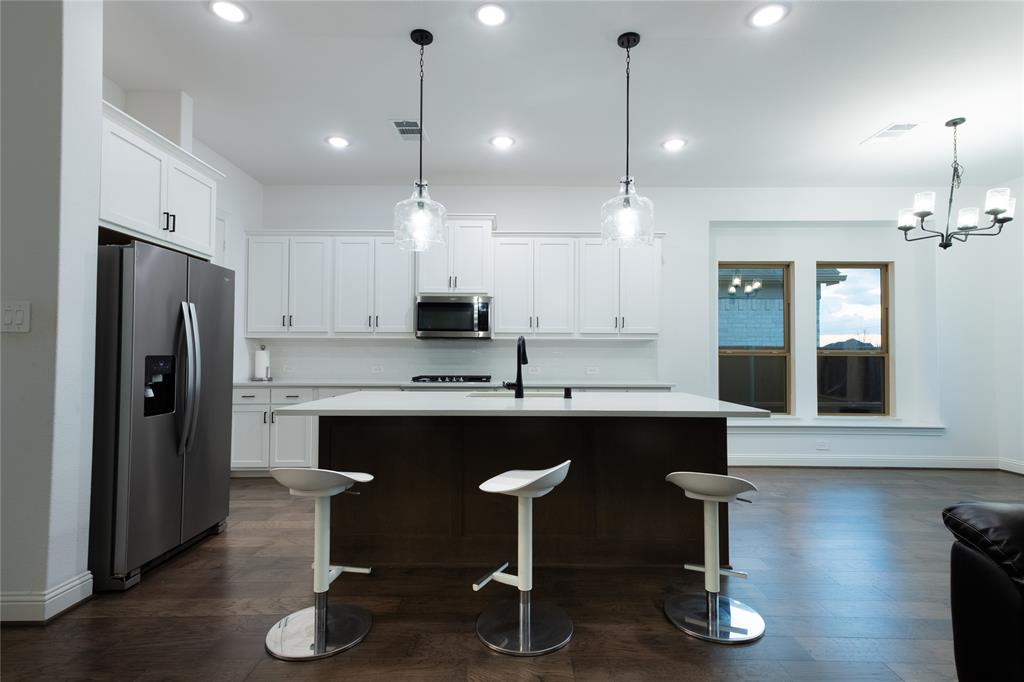 Kitchen featuring white shaker-style cabinetry, central island with a solid surface countertop, stainless steel refrigerator, dark wood-finish flooring, and recessed ceiling lighting