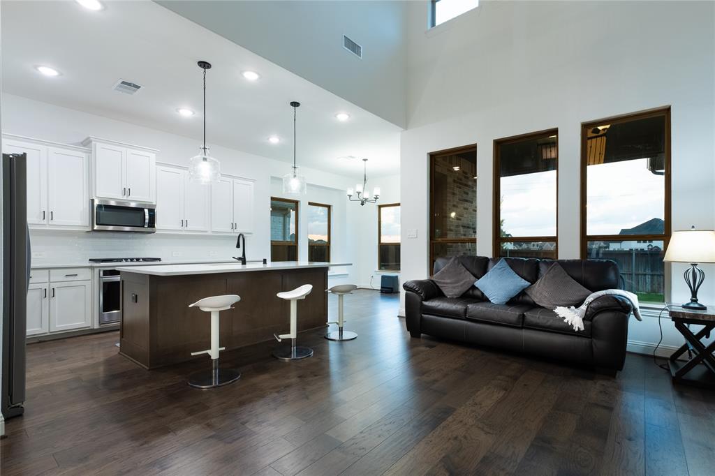 Open-concept living space featuring high ceilings, wood-finish flooring, white cabinetry, a kitchen island with a stone-finish countertop, and large windows