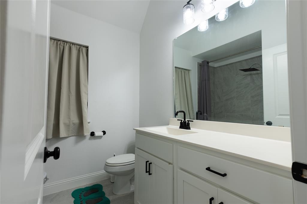 Bathroom featuring a white vanity with matte black hardware, a solid-surface countertop with an integrated sink, a large wall-mounted mirror, and a multi-bulb vanity light fixture