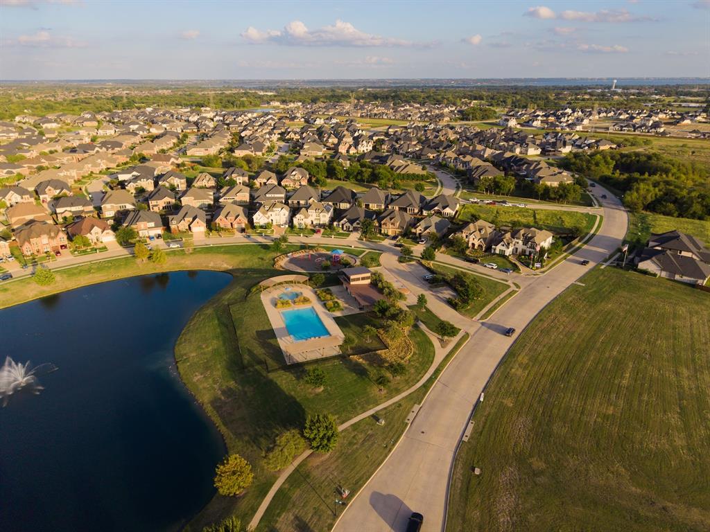 Aerial perspective of a community featuring a fenced swimming pool, central water feature with a fountain, paved walking paths, and designated open green space