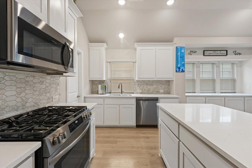 Kitchen featuring white shaker cabinetry, a central island with a quartz countertop, stainless steel appliances, and a hexagon-patterned stone backsplash