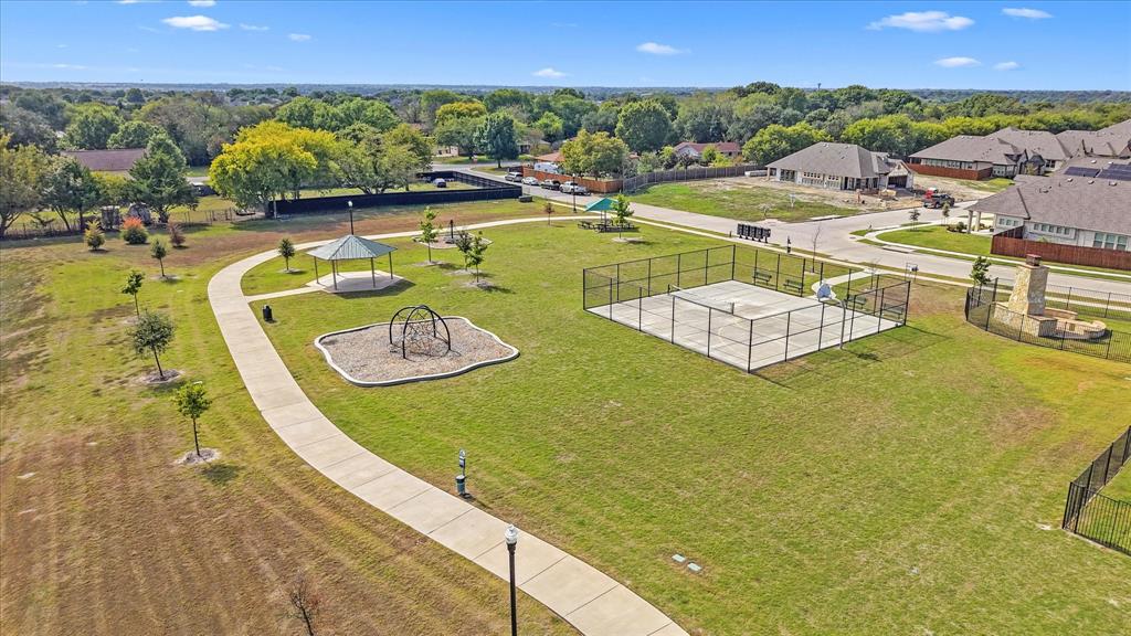 Community park featuring a fenced sports court, a covered gazebo, a paved walking path, and open green space
