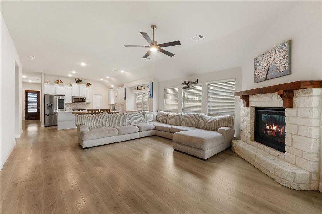 Vaulted ceilings with recessed lighting, stone fireplace featuring a prominent wooden mantel, wood-finish flooring, and white cabinetry