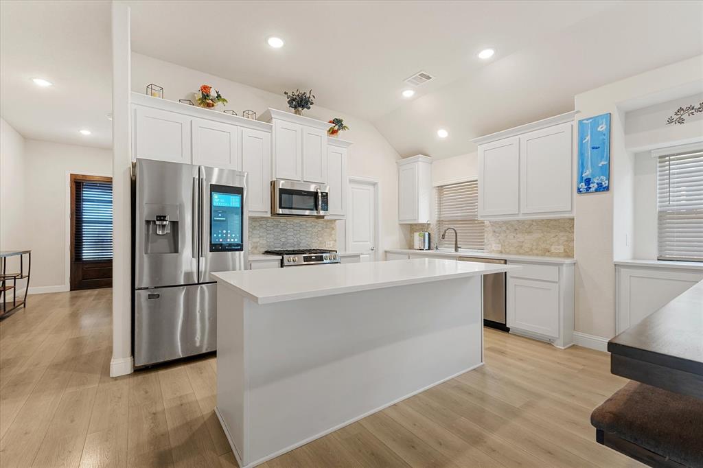 Kitchen featuring white shaker-style cabinetry, a central island with a solid surface countertop, stainless steel appliances, wood-finish flooring, and recessed lighting