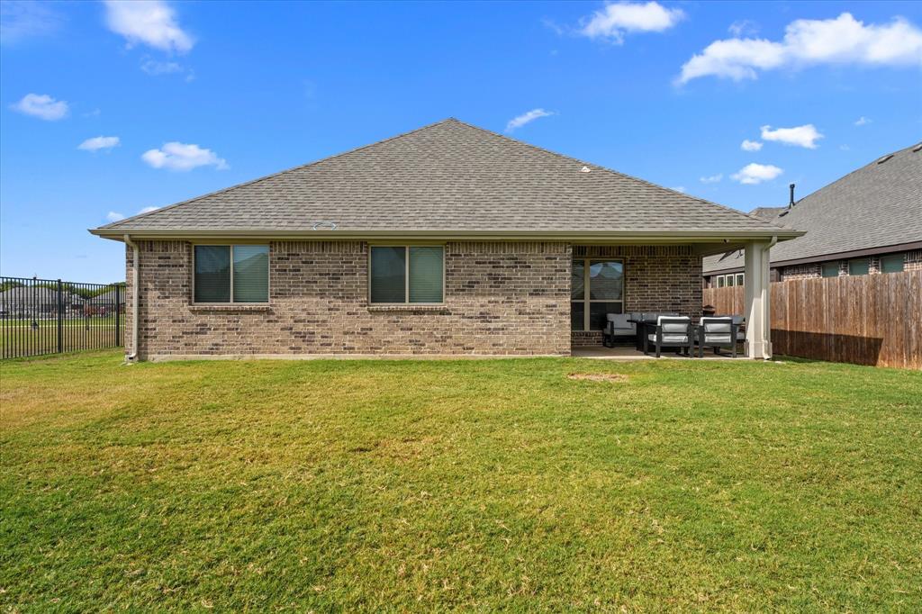 Rear brick exterior featuring a covered patio, a grass lawn, and wood-slat fencing