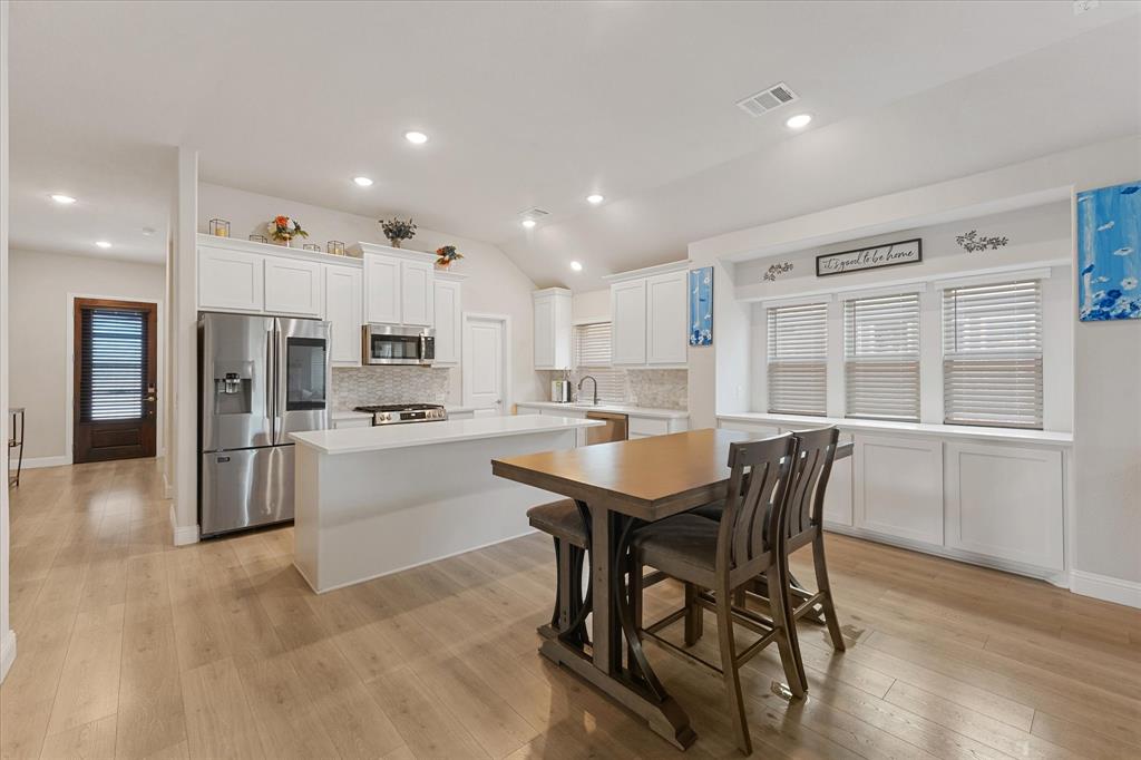 Kitchen featuring white shaker-style cabinetry, quartz countertops, stainless steel appliances, wood-finish flooring, and built-in window seating with lower storage