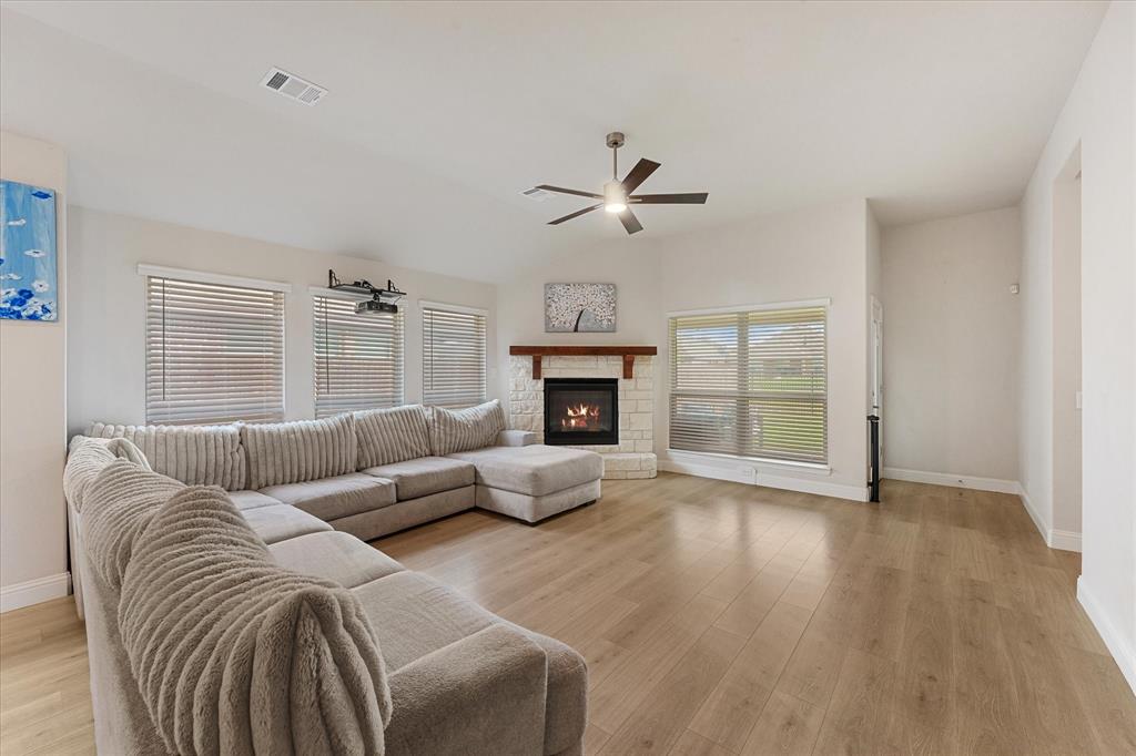Living area featuring wood-finish flooring, vaulted ceilings, a stone-surround fireplace with a timber mantel, and an integrated ceiling fan