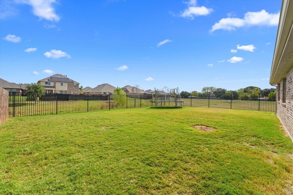 Expansive backyard featuring a large grass lawn, perimeter black metal fencing, and brick exterior siding