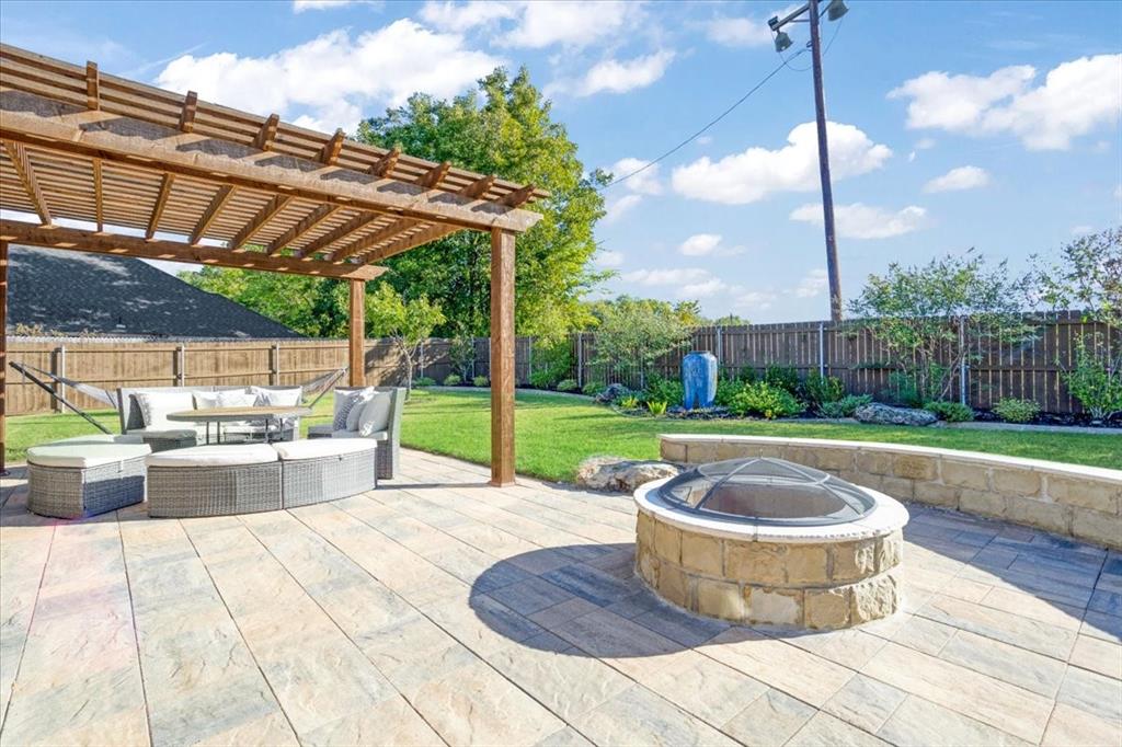 Backyard featuring a paved stone patio, a wooden pergola, a circular stone fire pit with a masonry seating wall, and a wood privacy fence