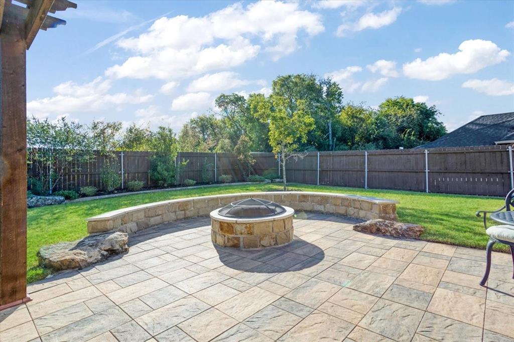 Backyard featuring a paved stone patio, built-in natural stone fire pit, curved stone seating wall, and wood privacy fencing