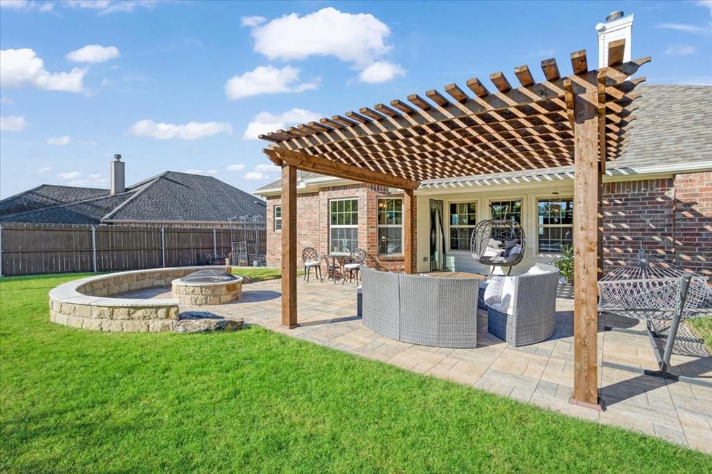 Backyard featuring a custom wood-beam pergola, stone-paver patio, and built-in stone fire pit with a curved retaining wall