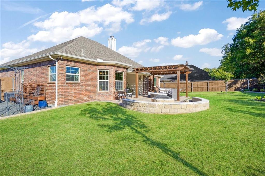 Brick exterior residence featuring a covered pergola, stone-accented fire pit, paved patio, and fenced backyard