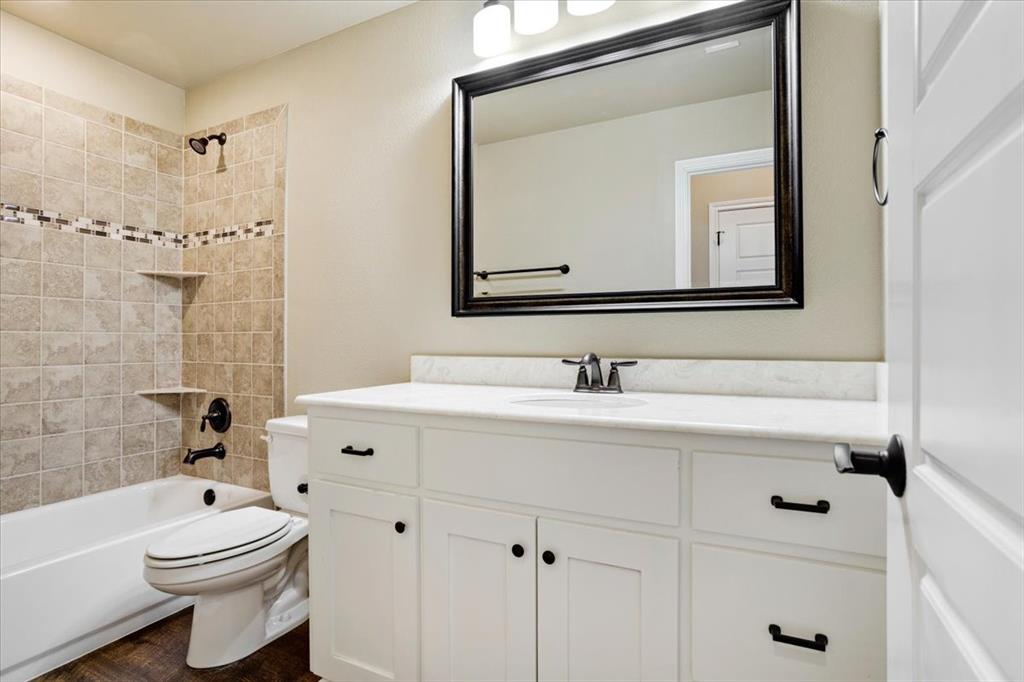 White vanity cabinet with quartz countertop, undermount sink, and matte black hardware, paired with a shower-tub combination featuring tiled walls with a decorative accent border and matte black fixtures
