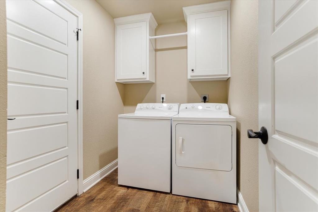 Laundry area featuring white shaker-style wall cabinets, a built-in hanging rod, four-panel interior doors, and wood-finish flooring