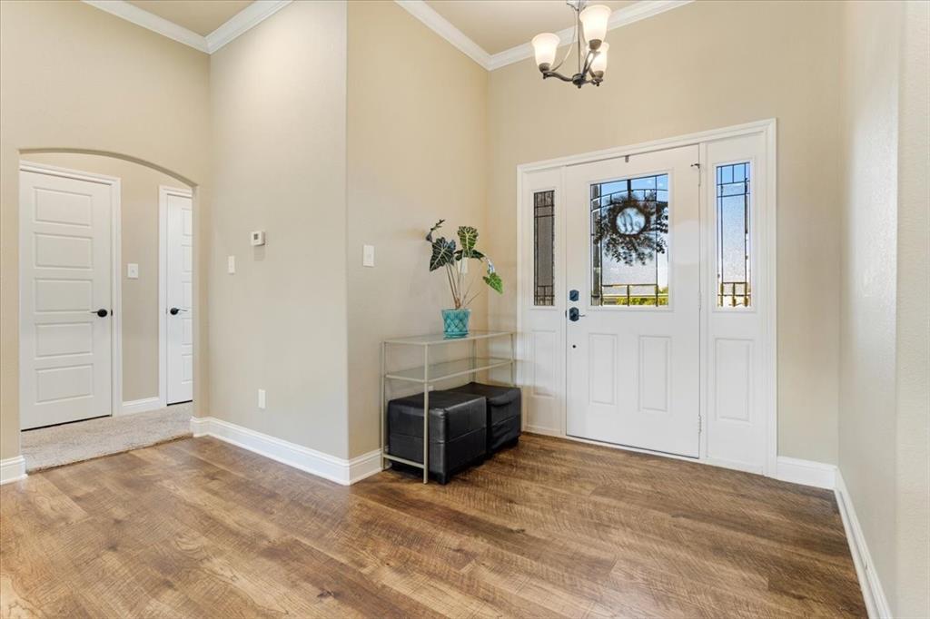 Entryway featuring wood-finish flooring, high ceilings with crown molding, an arched interior passageway, and a white front door with sidelights
