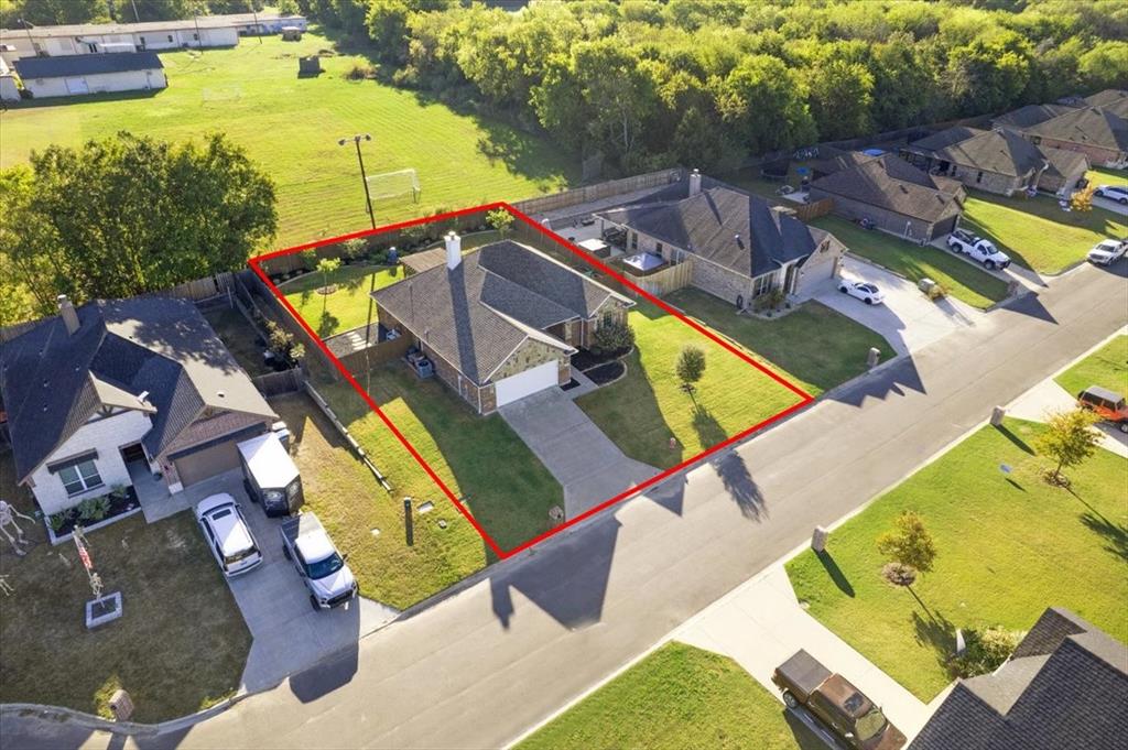 Aerial perspective of a single-story residence featuring a brick and stone exterior, a gabled roofline, an attached front-facing garage, and a fenced backyard