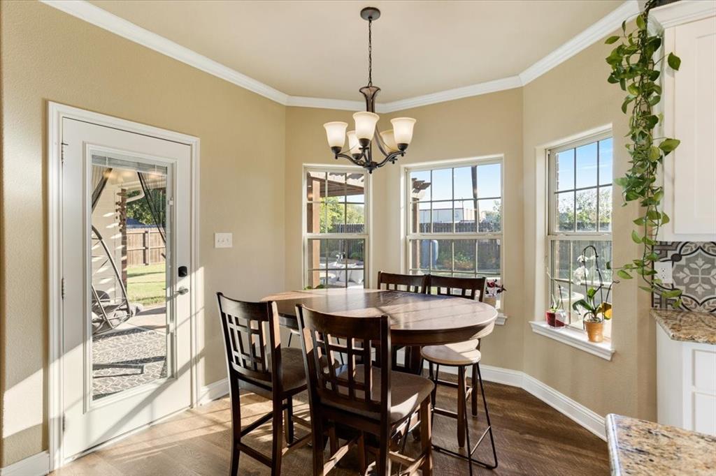 Bay window featuring three paneled windows, wood-finish flooring, white crown molding, a multi-light chandelier, and a glass-paneled exterior door
