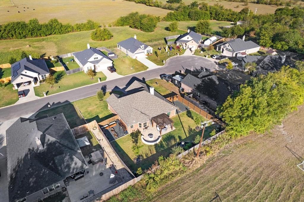 Aerial perspective featuring a single-story residence with a composite shingle roof, a backyard with a stone-surfaced fire pit, a wood-frame pergola, and a concrete patio