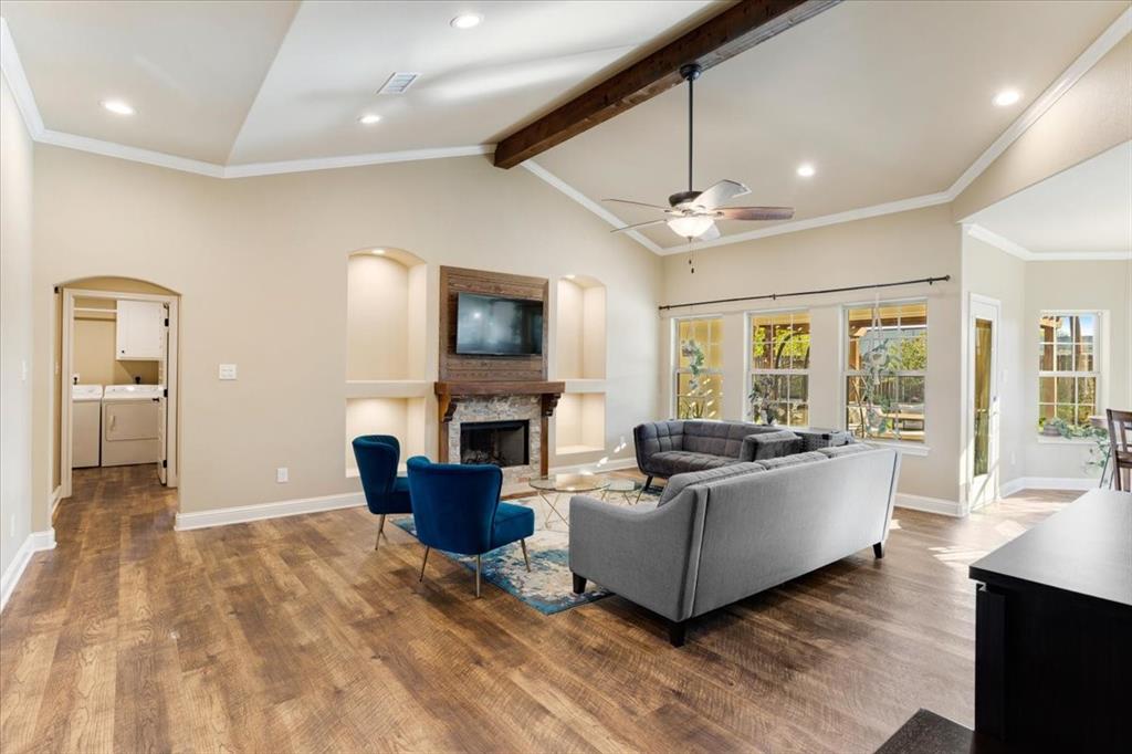 Vaulted ceilings featuring a stained wood beam, wood-finish flooring, stone-surround fireplace with a custom wood mantel, and built-in recessed shelving
