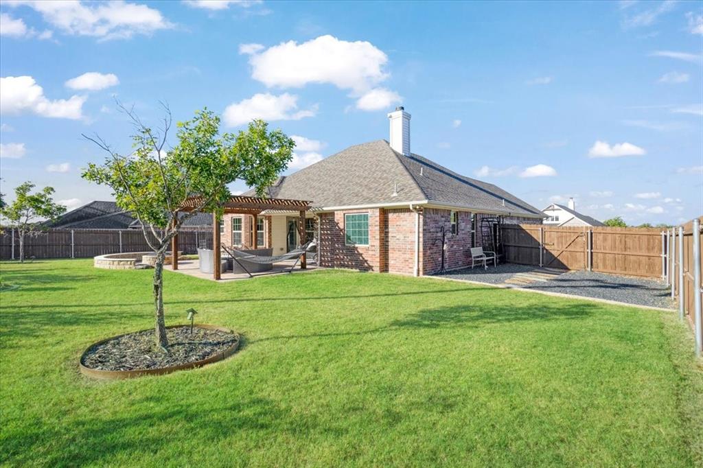Expansive backyard featuring a brick exterior, covered wooden pergola, stone-lined fire pit, and full perimeter wood fencing