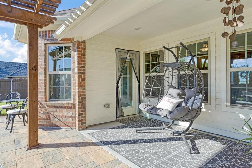 Covered rear patio featuring horizontal lap siding, brick masonry detailing, a timber pergola, and stone-finish tile flooring