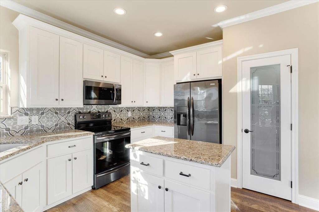 White cabinetry with stone countertops, patterned tile backsplash, stainless steel appliances, wood-finish flooring, and a glass-paneled interior door
