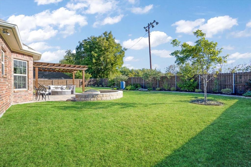 Backyard featuring a brick-exterior home, a wood pergola, a stone-surround fire pit, and a fenced perimeter