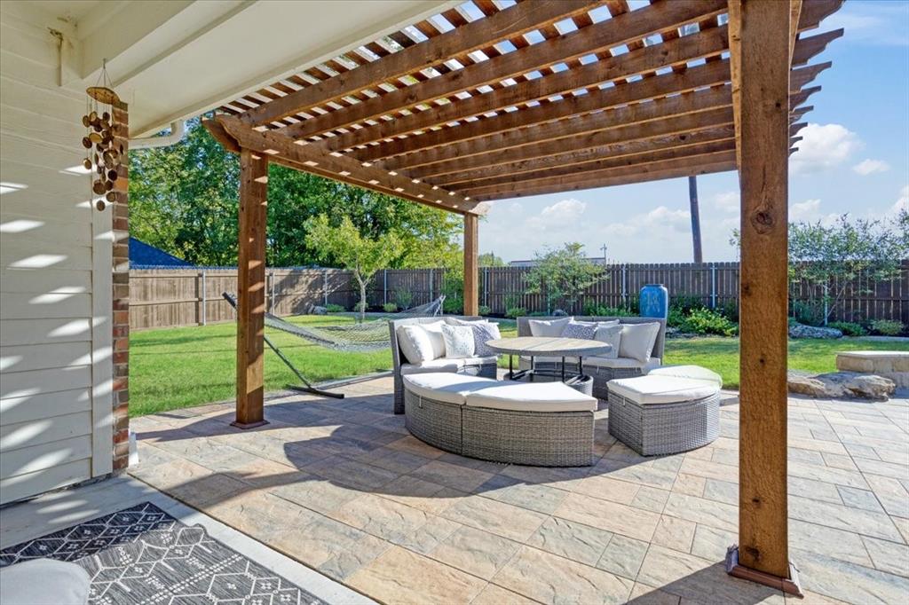 Covered patio featuring a timber-frame pergola, natural stone-finish pavers, a stone landscape border, and a fenced backyard