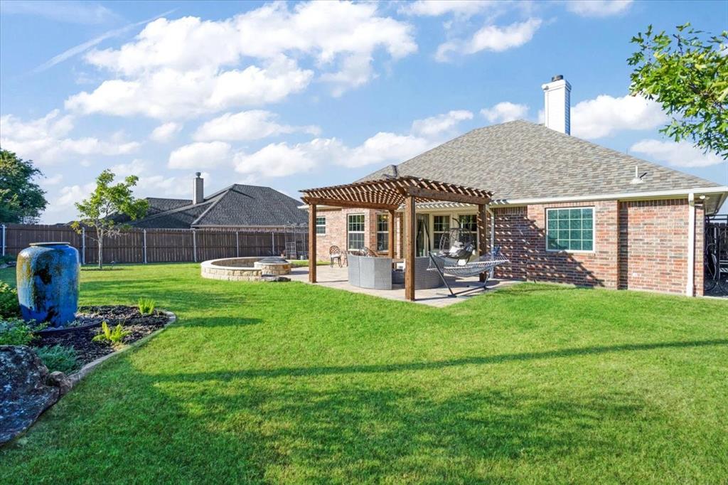 Brick exterior residence featuring a wooden pergola, concrete patio, stone fire pit, and expansive lawn