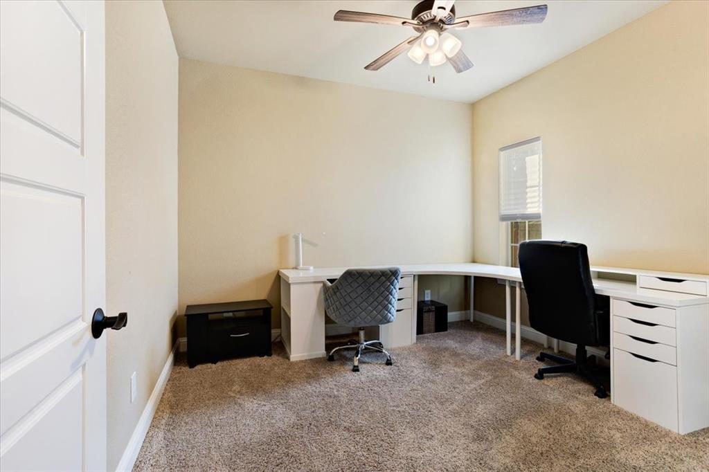 Neutral-toned interior room featuring wall-to-wall carpeting, a multi-blade ceiling fan with integrated lighting, a single-panel interior door with matte black hardware, and a window with fitted blinds