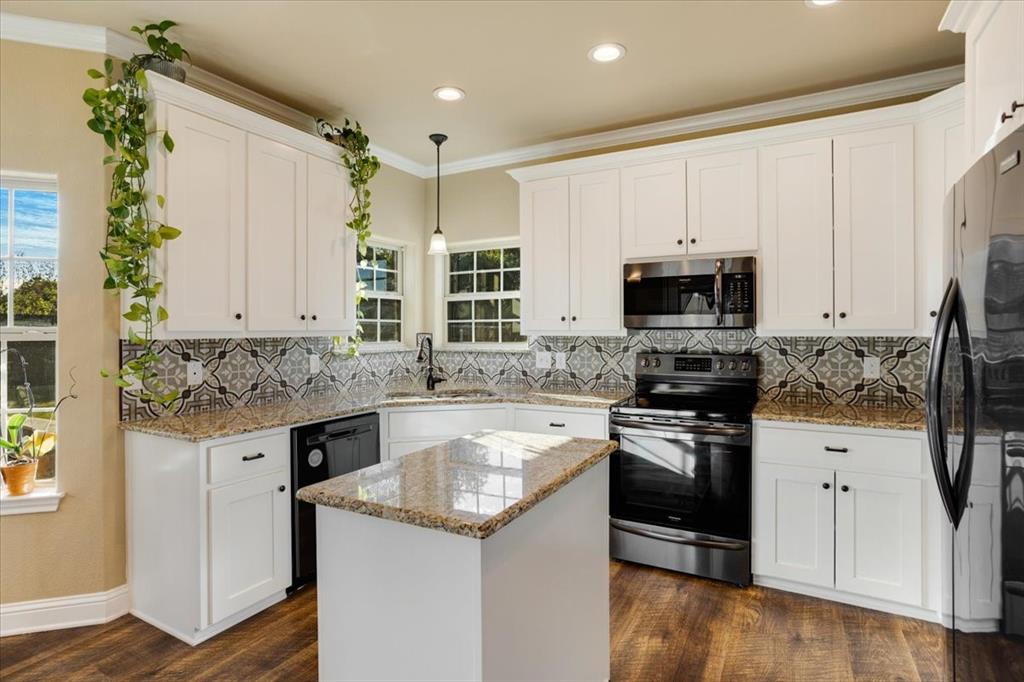 Kitchen featuring white shaker cabinetry, stone countertops, patterned tile backsplash, wood-finish flooring, and a central island