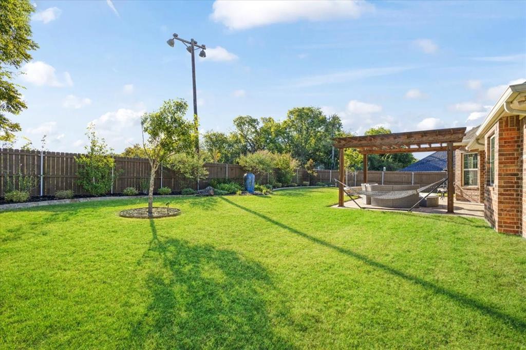 Expansive backyard featuring a wood-beam pergola, brick exterior siding, manicured lawn, and perimeter wood fencing