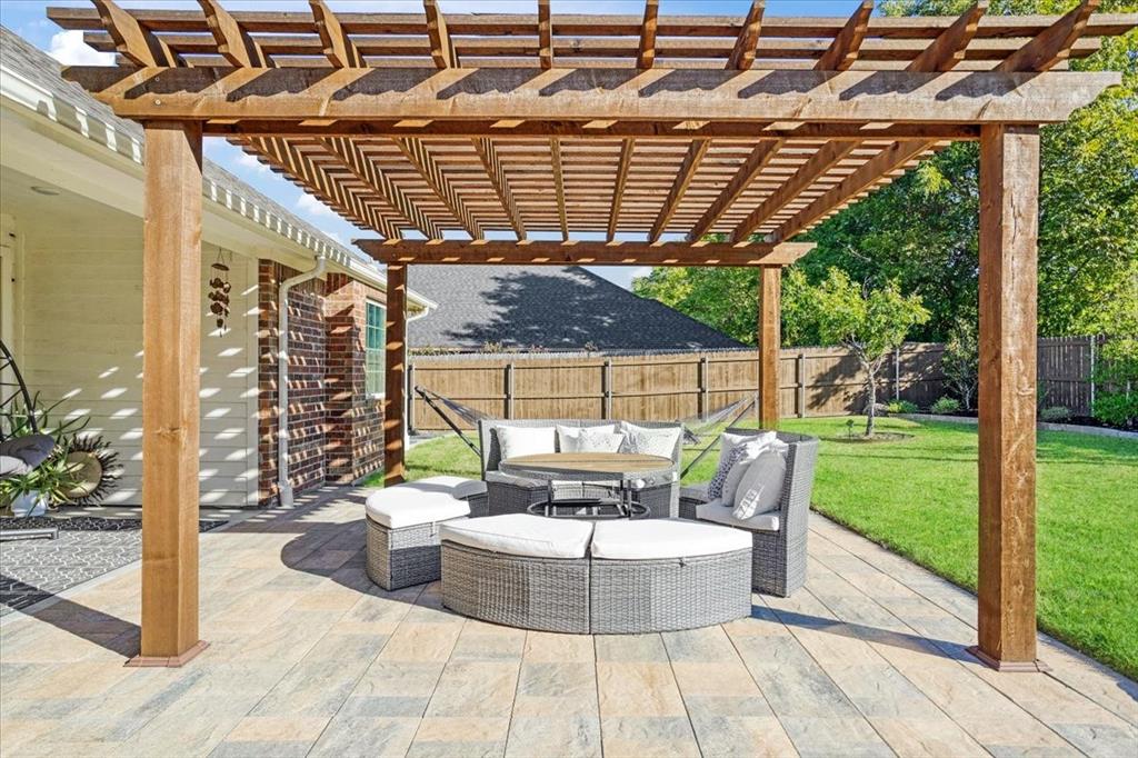 Custom wood pergola featuring a slatted roof design atop an expansive stone paver patio, complemented by a fenced backyard and brick exterior siding