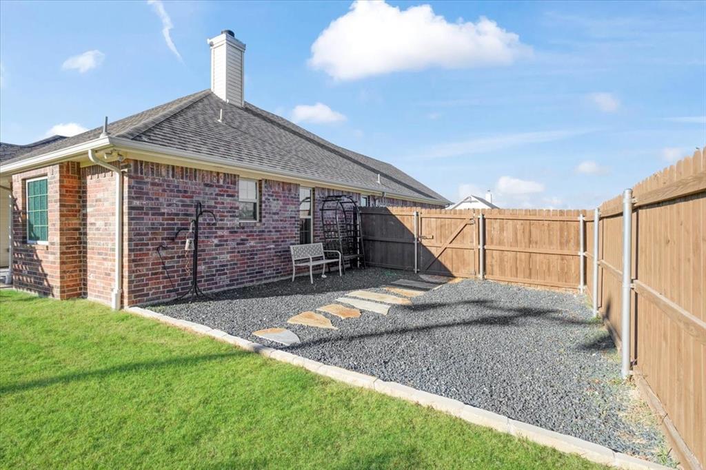 Brick exterior with a chimney, stone paver pathway, gravel ground cover, and a wood privacy fence