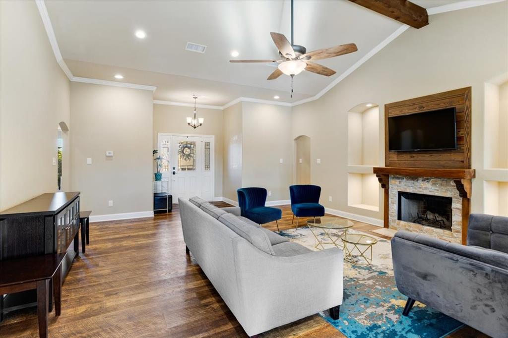 Vaulted ceiling featuring a central ceiling fan, wood-finish flooring, stone-surround fireplace with a timber mantel, and custom recessed wall niches