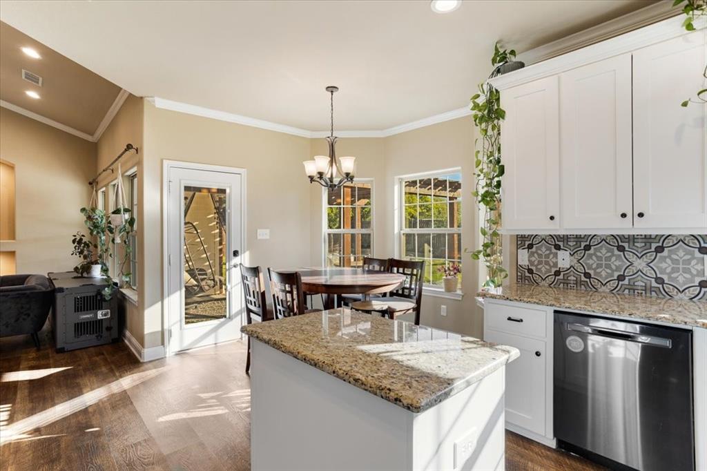 Kitchen featuring white cabinetry, stone countertops, patterned tile backsplash, stainless steel dishwasher, and wood-finish flooring