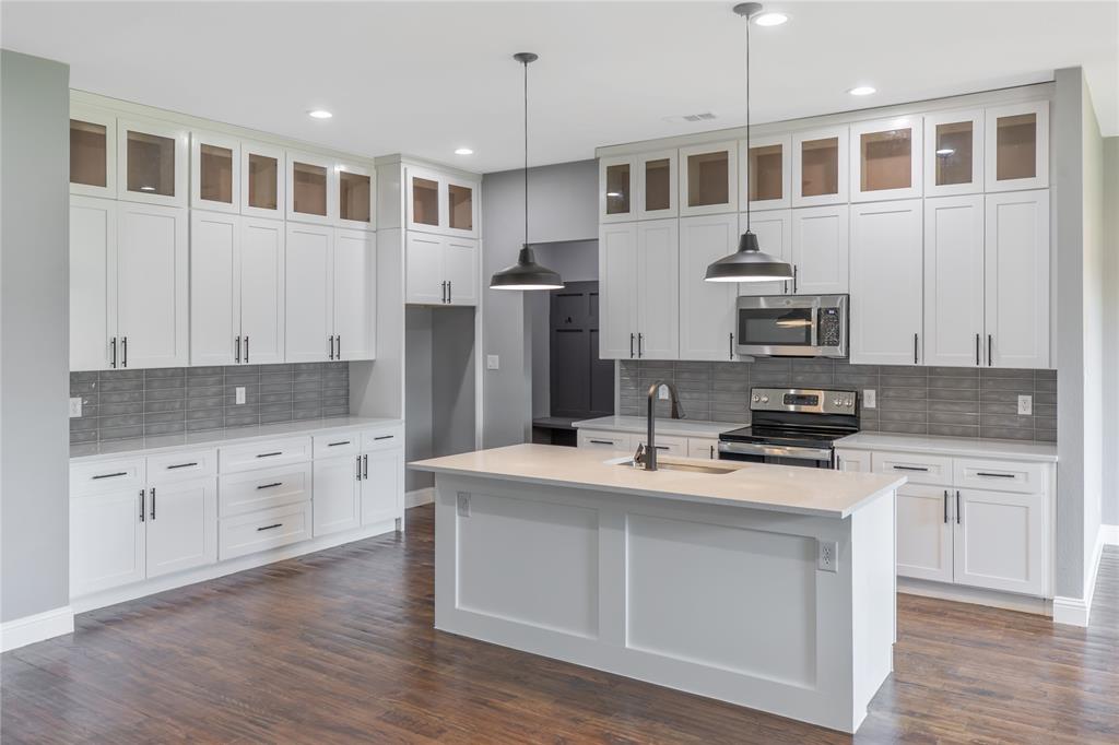 Kitchen featuring appliances with stainless steel finishes, glass insert cabinets, hanging light fixtures, tasteful backsplash, and dark wood finished floors