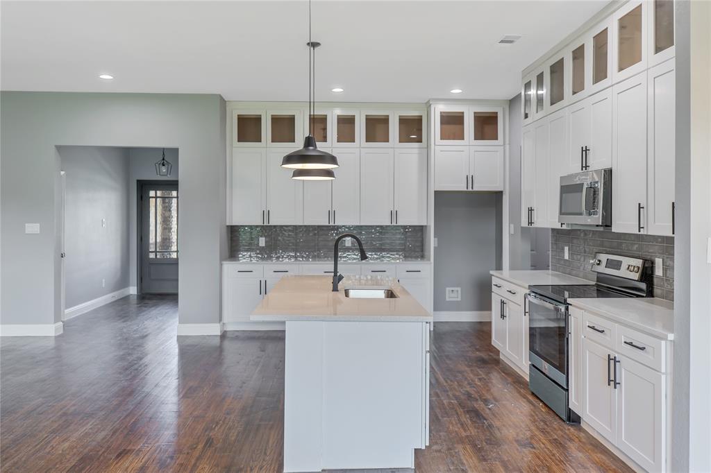 Kitchen with stainless steel appliances, pendant lighting, a center island with sink, tasteful backsplash, and light stone countertops