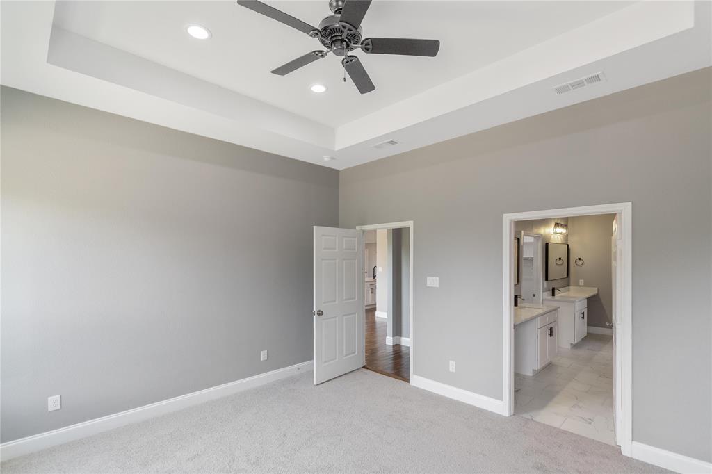 Unfurnished bedroom with a tray ceiling, light carpet, a ceiling fan, connected bathroom, and recessed lighting