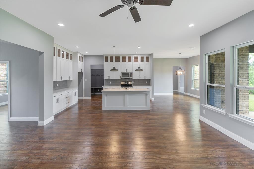 Kitchen featuring tasteful backsplash, glass insert cabinets, a center island with sink, dark wood finished floors, and ceiling fan