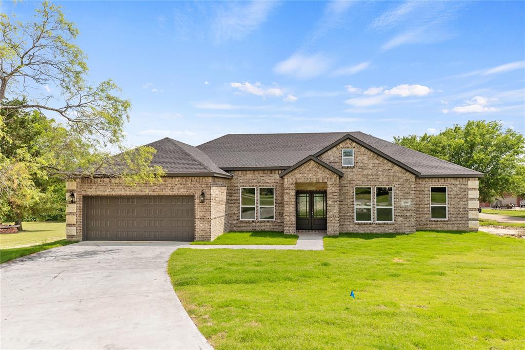 View of front facade with a shingled roof, a front lawn, brick siding, concrete driveway, and french doors