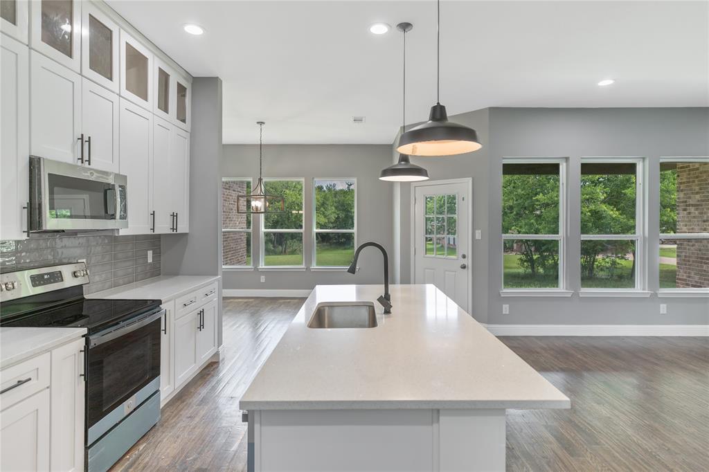 Kitchen with appliances with stainless steel finishes, an island with sink, white cabinets, light stone counters, and tasteful backsplash