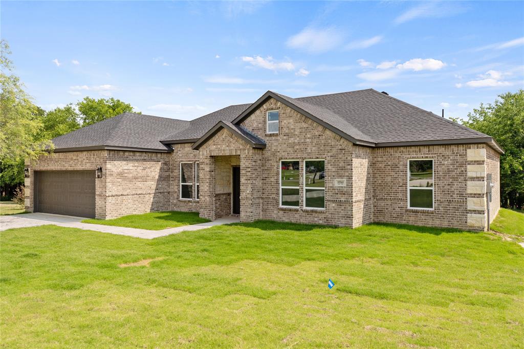 View of front of house featuring a front yard, brick siding, roof with shingles, a garage, and driveway