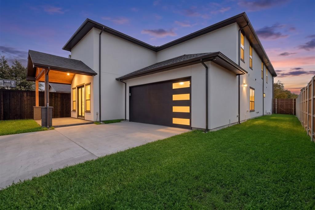 Modern two-story exterior featuring smooth stucco siding, a covered patio with wood-finish ceiling, and a multi-panel garage door with horizontal light inserts