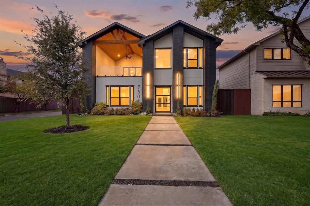 Modern exterior featuring dark masonry, a covered balcony with wood-paneled ceiling, integrated vertical lighting, and a paved walkway with stone aggregate detailing