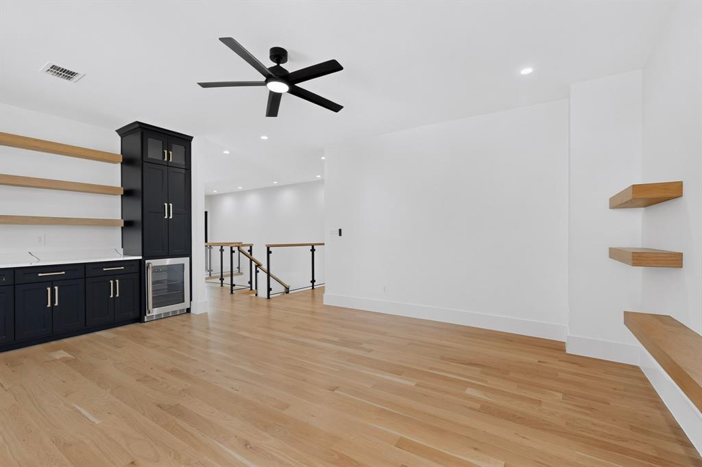 Wood-finish flooring, custom black cabinetry with built-in beverage refrigerator, natural wood floating shelves, and matte black ceiling fan