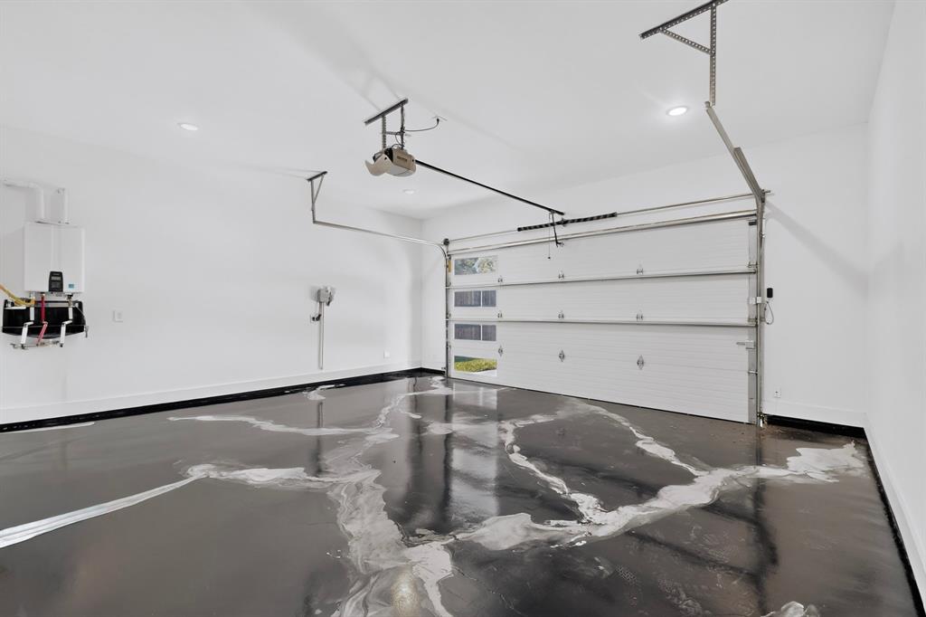 Garage interior featuring high-gloss epoxy flooring, white paneled door with integrated glass windows, tankless water heater, and recessed lighting