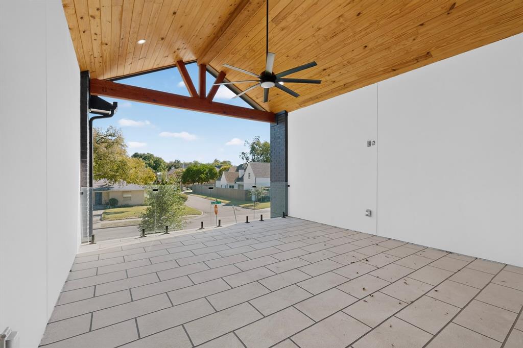 Covered balcony featuring a wood-plank vaulted ceiling, tiled flooring, exposed timber beam, and frameless glass railing with industrial-style standoffs